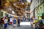 Calle peatonal de Praga con árboles otoñales, tiendas y gente paseando.