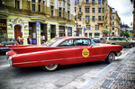 Coche clásico rojo en una avenida de Praga con edificios históricos al fondo.