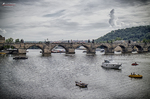 Puente de Carlos sobre el río Moldava con barcas y cielo gris en Praga.