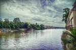 Ribera del Moldava en Praga con árboles, edificios y cielo dramático.