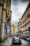 Calle estrecha de Praga con coches aparcados, fachadas históricas y cielo nublado.