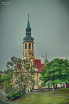 Torre de iglesia con aguja verde entre árboles en Praga.