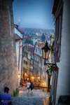 Calle estrecha y empinada de Praga al anochecer con luces cálidas.