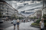 Avenida o plaza de Praga con peatones, edificios modernos y cielo dramático.