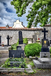 Cementerio antiguo de Kutná Hora con lápidas, vegetación y muro blanco al fondo.