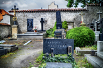 Tumba destacada en un cementerio de Kutná Hora con edificio blanco al fondo.