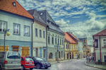 Calle tranquila de Kutná Hora con casas de colores, coches y cielo azul.