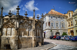 Fuente gótica de piedra en una plaza de Kutná Hora con edificios históricos.