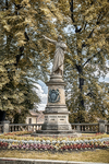 Monumento en un parque de Kutná Hora rodeado de flores y árboles de otoño.
