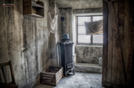 Celda o habitación deteriorada de Terezín con estufa, ventana y paredes desgastadas.