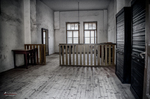 Sala interior vacía de Terezín con ventanas, barandilla y suelo de madera.