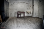 Habitación austera del antiguo campo de Terezín con mesa, cama y paredes desnudas.