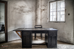 Sala de interrogatorio u oficina histórica de Terezín con mesa y ventana enrejada.