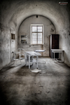 Habitación vacía de Terezín con mesa, silla y ventana bajo un arco.
