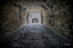 Túnel abovedado de piedra en Terezín con salida iluminada al fondo.
