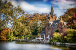 Paisaje de Brujas junto al agua con iglesia, casas de ladrillo y vegetación otoñal.