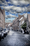 Calle empedrada de Brujas con casas blancas, tejados escalonados y cielo nublado.