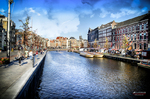Canal de Ámsterdam con barcas, edificios históricos y cielo azul reflejado en el agua.