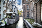 Canal estrecho de Ámsterdam entre edificios antiguos con barca y reflejos en el agua.