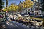 Paseo junto al canal de Ámsterdam con árboles, barcas amarradas y ambiente otoñal.