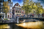 Puente sobre un canal de Ámsterdam con casas de colores, árboles y luz cálida.