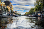 Canal de Ámsterdam con barcas, fachadas históricas y cielo abierto entre nubes.
