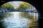 Canal de Ámsterdam visto desde debajo de un puente, con árboles y agua en perspectiva.