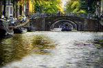 Puente de piedra sobre un canal de Ámsterdam con barcas y vegetación otoñal.