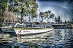 Barca blanca navegando por un canal de Ámsterdam con edificios y árboles al fondo.