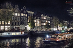 Canal nocturno de Ámsterdam con edificios iluminados y reflejos de luces en el agua.