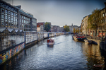 Canal amplio de Ámsterdam con edificios alineados, barcas y luz suave de otoño.