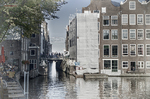Canal estrecho de Ámsterdam entre edificios altos con barcas amarradas y luz gris.