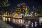 Canal nocturno de Ámsterdam con luces reflejadas en el agua y edificios junto al paseo.