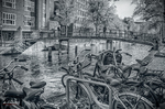 Puente y bicicletas junto a un canal de Ámsterdam en blanco y negro con ambiente nostálgico.