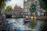 Canal de Ámsterdam con bicicletas en primer plano, barcas y casas de colores al fondo.