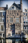 Casa estrecha tradicional de Ámsterdam junto al canal con fachada histórica y reflejo en el agua.