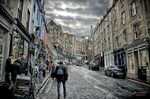 Calle estrecha de piedra en Edimburgo con peatones y edificios antiguos.