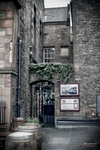 Entrada antigua de piedra en Edimburgo con puerta azul y carteles en la fachada.