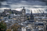 Panorámica de Edimburgo con rayos de luz entre nubes sobre la ciudad histórica.