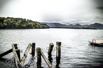 Paisaje de lago en Escocia con postes de madera, barcas y montañas entre niebla.
