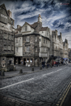 Calle histórica de Edimburgo con fachadas de piedra y cielo azul entre nubes.