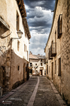 Calle estrecha de Pedraza entre fachadas de piedra y cielo nublado.