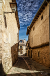 Calle estrecha de Pedraza entre muros de piedra y luz dorada.