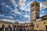Torre de iglesia en Pedraza sobre plaza de piedra y cielo dramático.