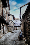 Calle empedrada de La Alberca con casas serranas y figura al fondo.