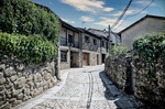 Calle empedrada de Sequeros con casas tradicionales, muros de piedra y árboles recortados.