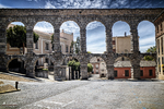Plaza bajo los arcos del Acueducto de Segovia con edificios históricos alrededor.