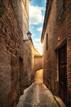 Callejón iluminado por luz cálida entre muros antiguos de Toledo.