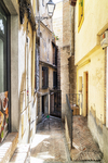 Callejón estrecho con luz intensa y fachadas antiguas en Toledo.