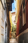 Calle estrecha con fachada rojiza y luz al fondo en Toledo.